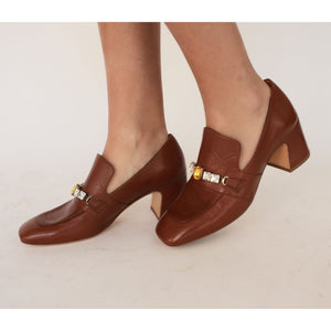 Brown leather mid-heel loafer worn by model; jewel buckle detail on vamp