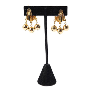 Gold clip-on earrings on black display, textured ear clips with three dangling balls