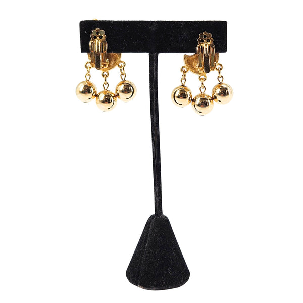 Gold clip-on earrings on black display, textured ear clips with three dangling balls