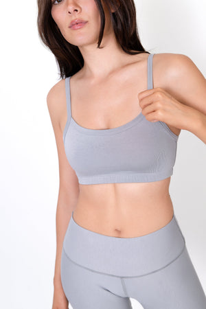 Gray sports bra with thin straps and scoop neckline, holding one strap