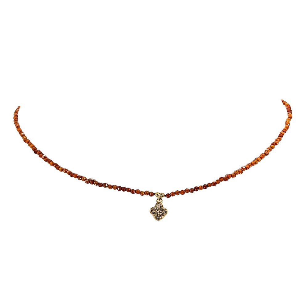 Orange beaded necklace with faceted beads and clover charm at center, silver clasp