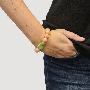 Peach-pink stretch bracelet with faceted green bead on wrist