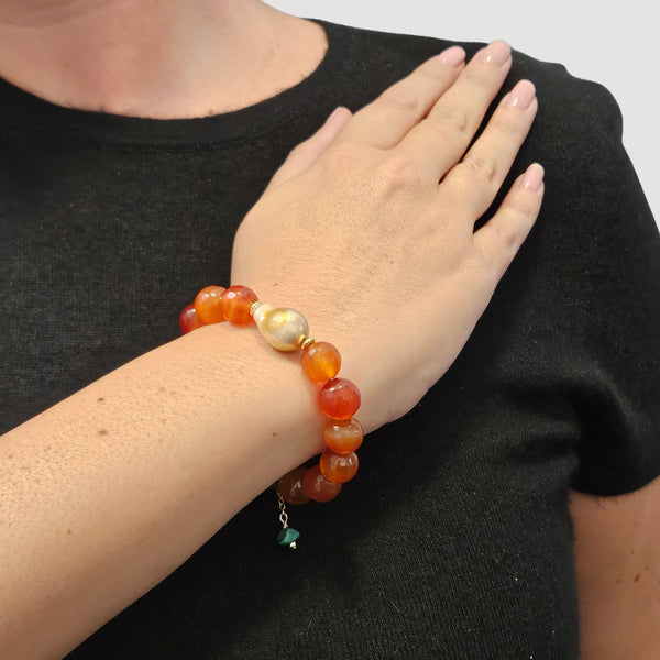 Red gemstone stretch bracelet on arm with pale pearl detail and green dangle charm