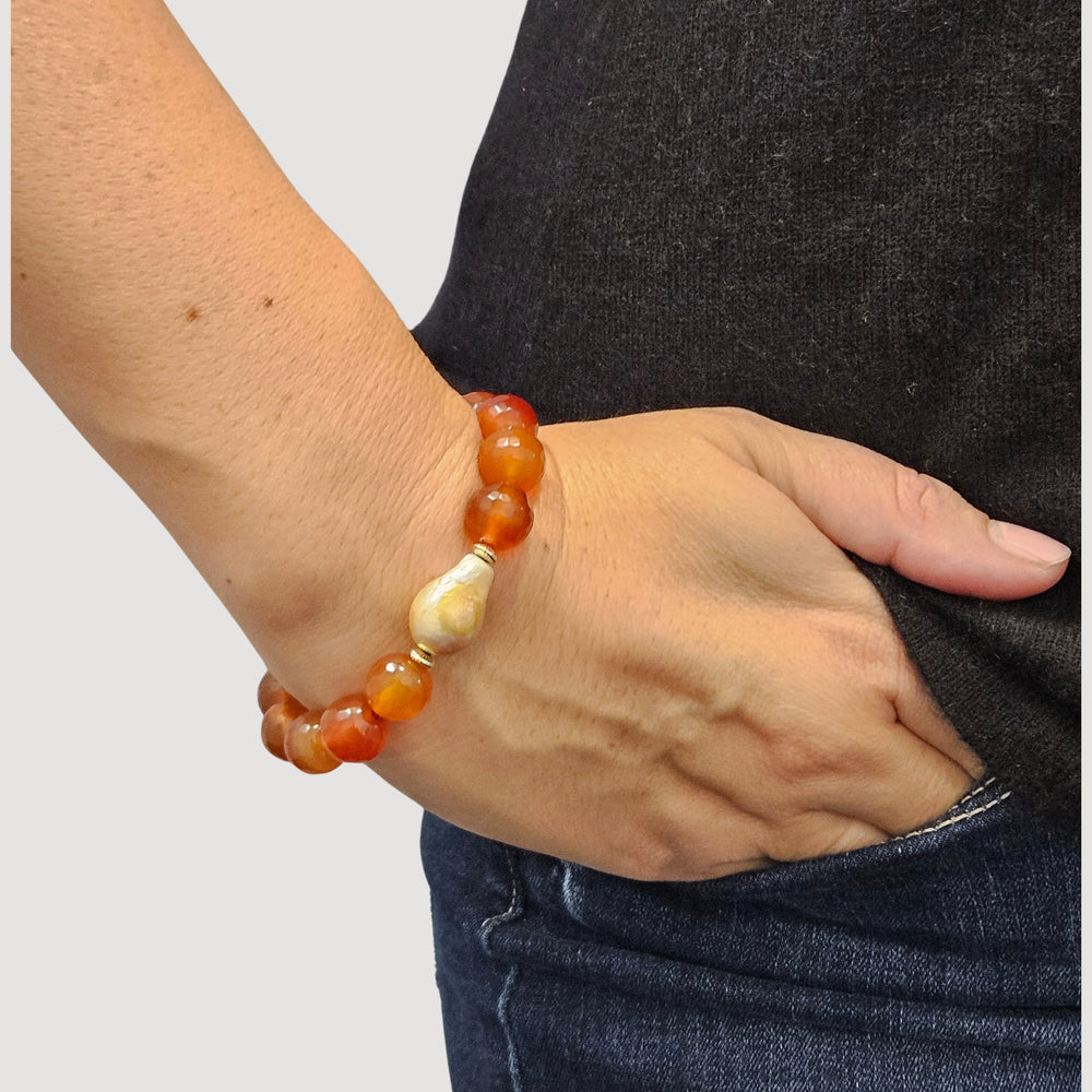 Stretch gemstone bracelet with red faceted beads, pale pearl spacer, and green dangle charm