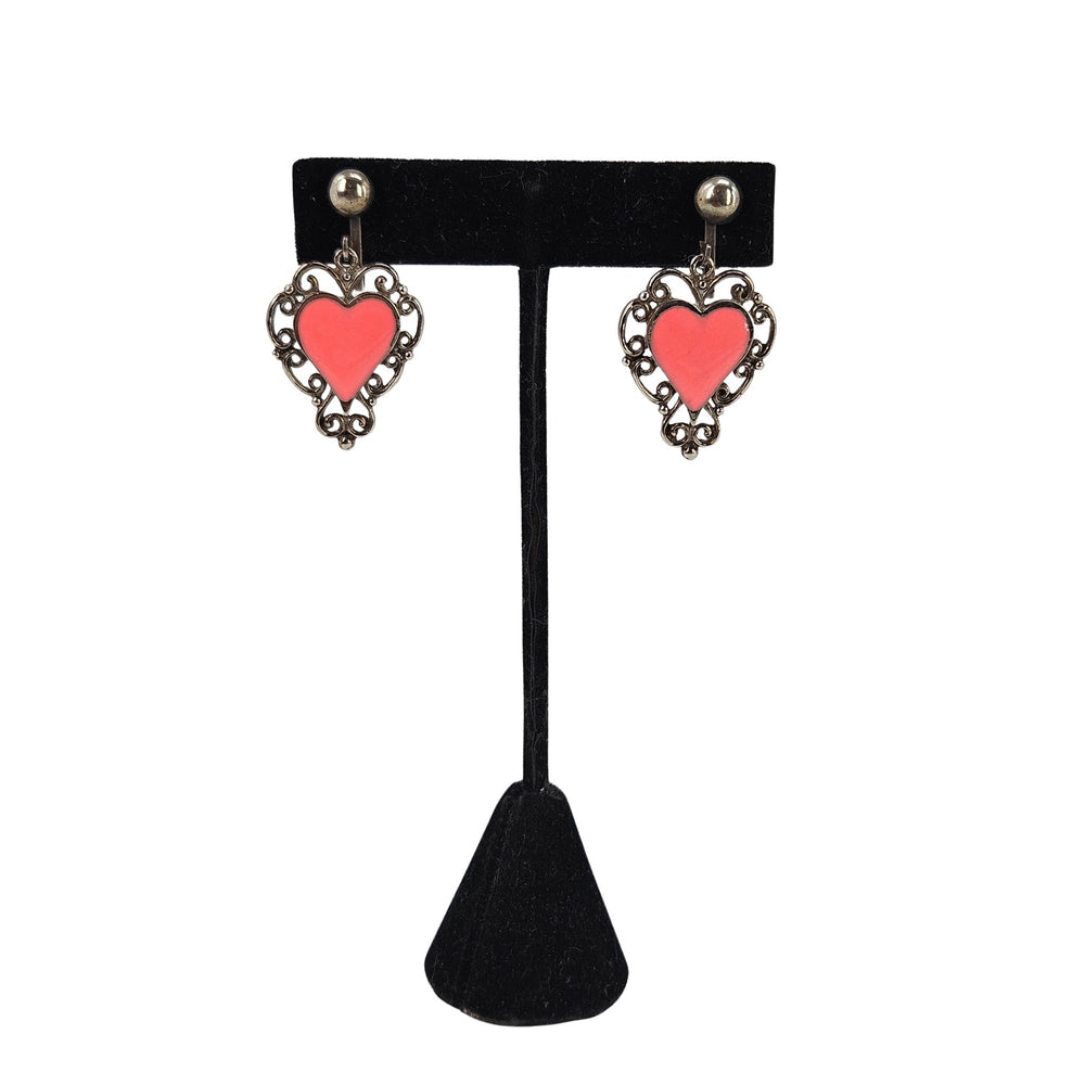 Gold-tone heart dangle earrings with pink enamel heart and ornate filigree frames.