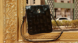 Black woven leather crossbody bag with front flap, gold lock clasp, adjustable strap