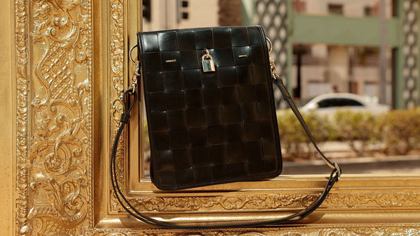 Black woven leather crossbody bag with front flap, gold lock clasp, adjustable strap