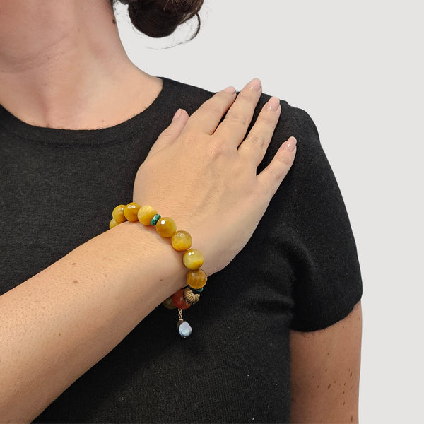 Yellow gemstone stretch bracelet with red bead, dark green spacers, and pearl drop