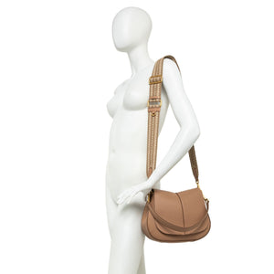 Small tan leather round shoulder bag on mannequin with crossbody strap and gold hardware