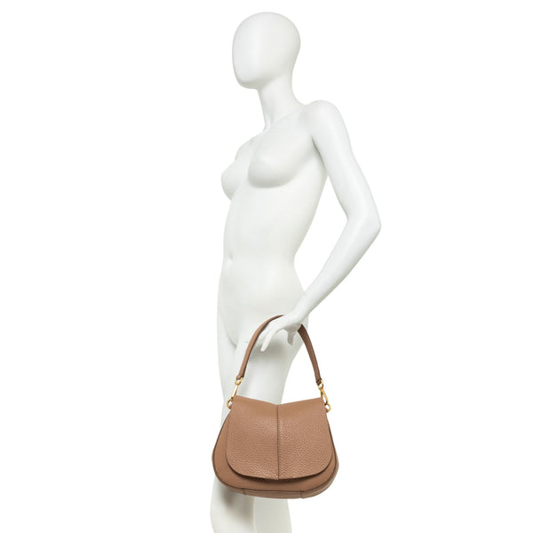 Tan leather half-moon shoulder bag held at side on mannequin with short crossbody strap