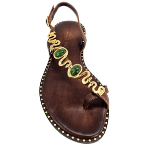 Dark brown leather flat sandal with open toe, gold serpent ornament and green stones