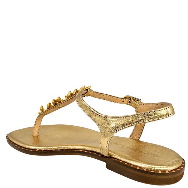 Gold flat sandal with toe thong strap and gold leaf accents along top strap