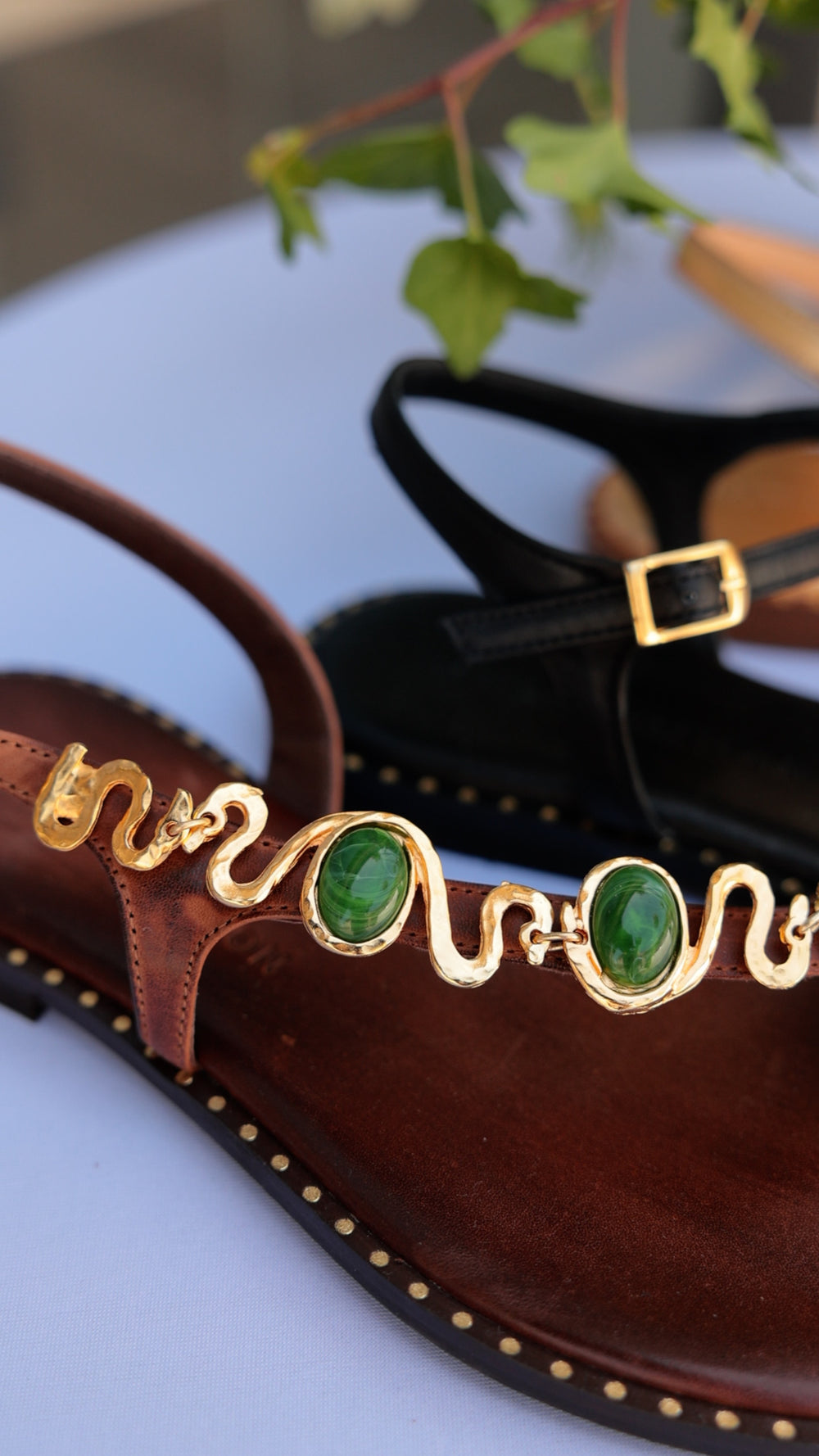 Madison Maison gold serpent chain flat sandal with green malachite cabochons on chocolate leather, brass studded sole, black hammered hardware sandal behind.