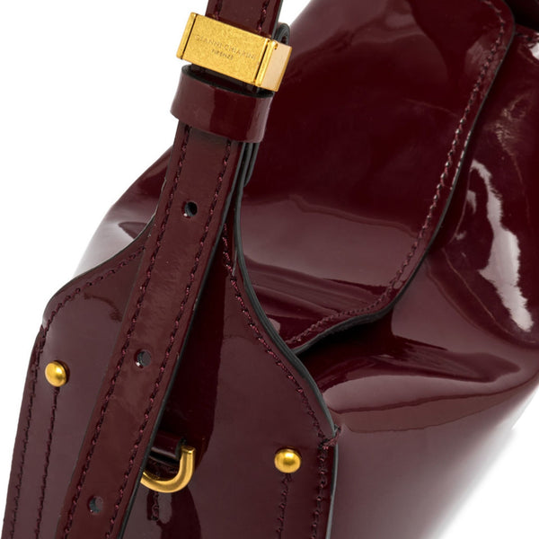 Dark berry patent-leather handbag detail with gold clasp, strap hardware, and stitching