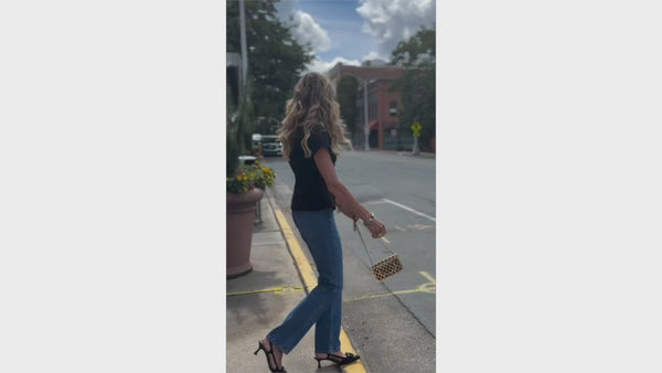 Woman in black top and blue jeans walking on a street with a white car in the background.