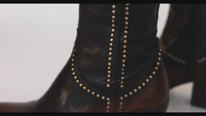 The Studded Western Ankle Boot in motion: the brown on the leg and the brown and black pair on the table, filmed at Madison Maison