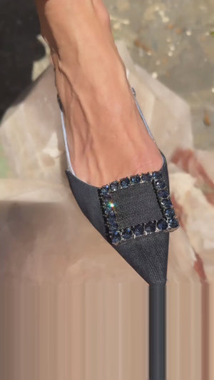 Pointed-toe slingback flat with low heel, adjustable ankle strap, and large decorative jewel embellishment on the toe. Features mixed material textures and an open heel design.