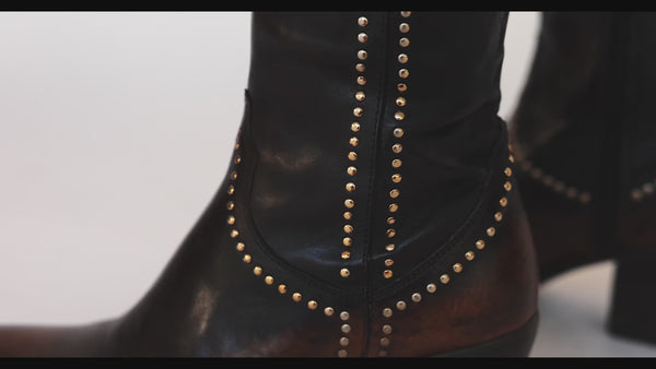 The Studded Western Ankle Boot in motion: the brown on the leg and the brown and black pair on the table, filmed at Madison Maison