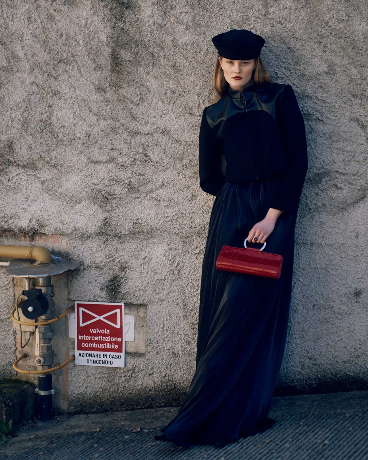 Woman in a long dark coat and red handbag against a textured wall.