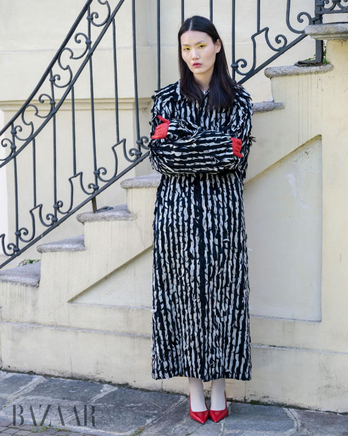 Woman in a patterned dress standing on steps with a Harpers Bazaar logo in the corner.