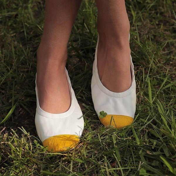 White ballet flats with yellow calf-hair toe tips on feet on grass